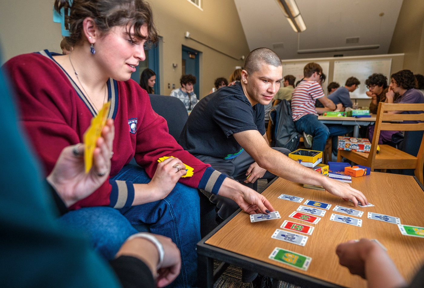 An image of 2 students playing a card game on a coffee table. 